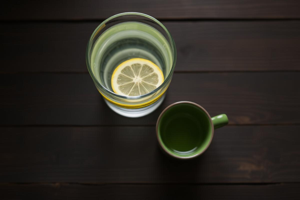 Vaso de agua con limón y taza de té verde sobre madera oscura